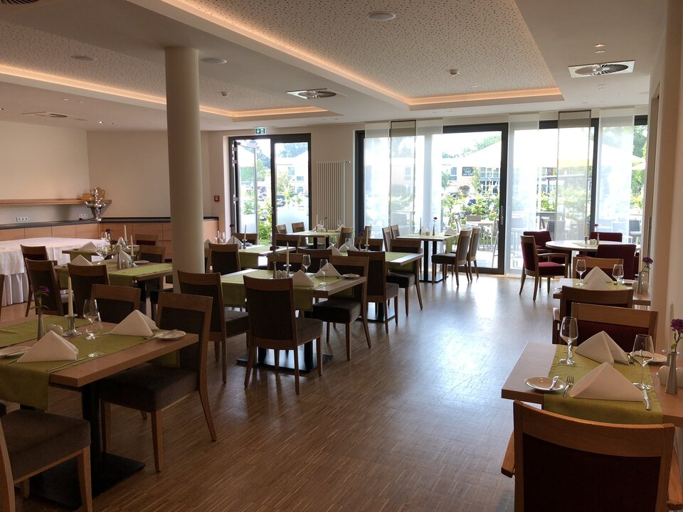 Ein modernes Restaurant mit warmen Farben, Holzböden und großen Fenstern, mit gedeckten Tischen und einem Barbereich im Hintergrund.